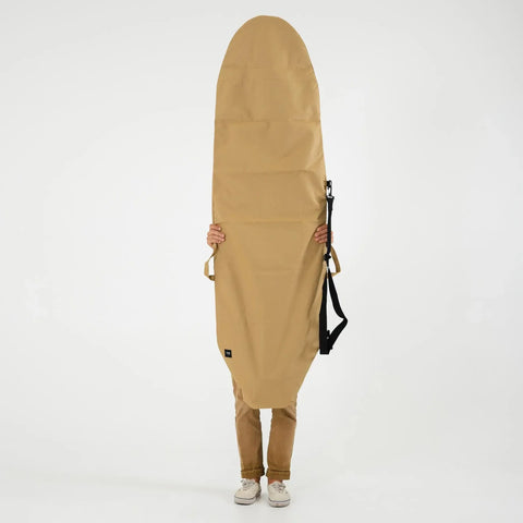 Person holding a tan surfboard bag on a white background