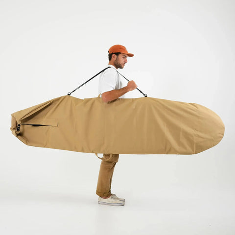 Man carrying a large beige surfboard bag on a white background