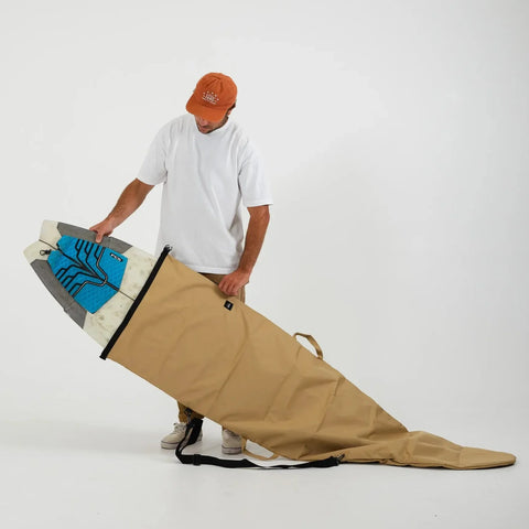 Person holding a large beige surfboard bag with a colorful surfboard inside on a white background