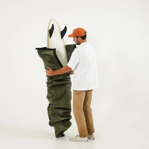Person holding a green bag with a surfboard inside on a white background
