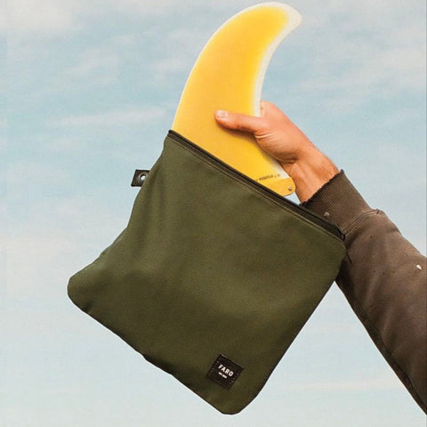 Person holding a green bag with a yellow fin against a blue sky background