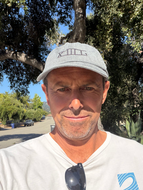 Man wearing a gray XIIIG dad hat cap and white shirt with sunglasses on a sunny day outdoors.