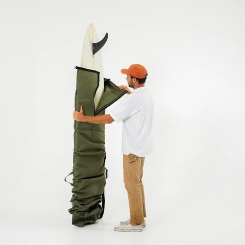 Man holding a large green bag with a white surfboard inside on a white background