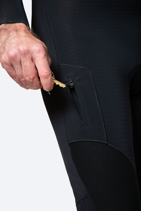 Close-up of the key pocket on the thigh of a 00 BY XIIIG wetsuit. The image is showing a man holding a key and putting it into the open thigh pocket