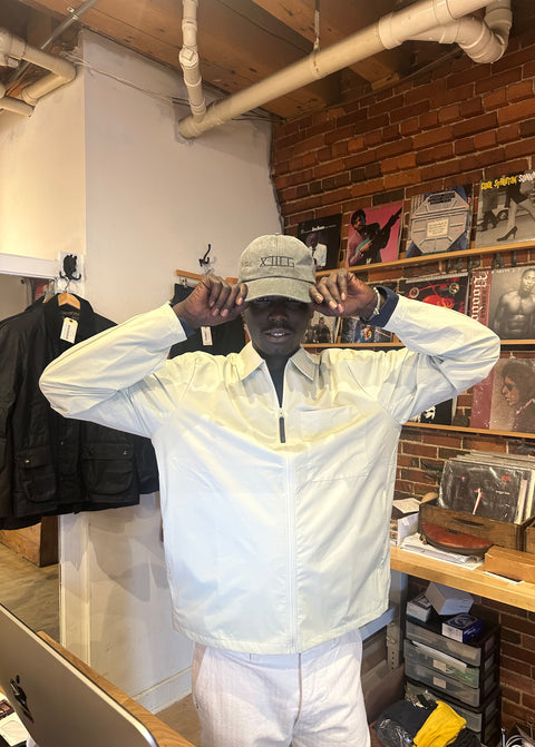 Person wearing the charcoal XIIIG dad hat and a white jacket in a store setting with records and clothing on display.