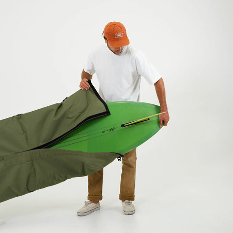 Man putting on an olive surfboard bag over a green surfboard against a white background