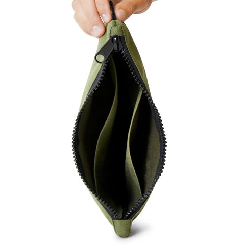 Green pouch with compartments with black YKK zipper held by a hand on a white background