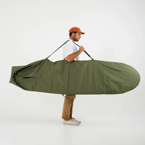 Man carrying a green surfboard bag on a white background