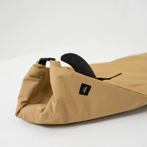 Tan surfboard bag with a black strap and a black fin showing while laying on a white background