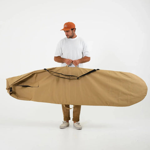 Man holding a large beige surfboard cover against a white background