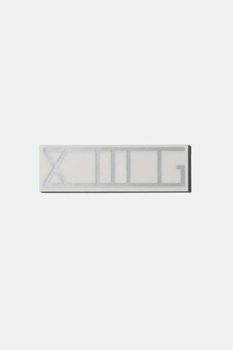 A shiny silver XIIIG sticker with a clear backing on a white background