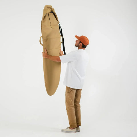 Person holding a large beige surfboard bag against a white background