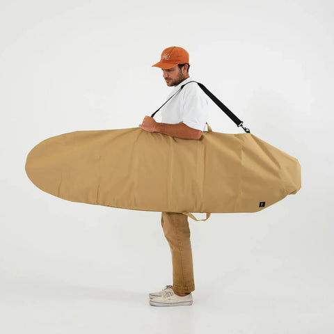 Man holding a large beige surfboard bag against a white background
